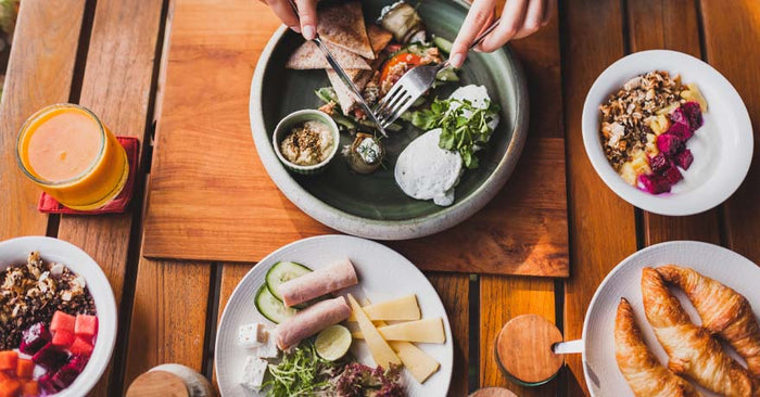 Multiple plates of food on a wooden table, hands eating from one plate